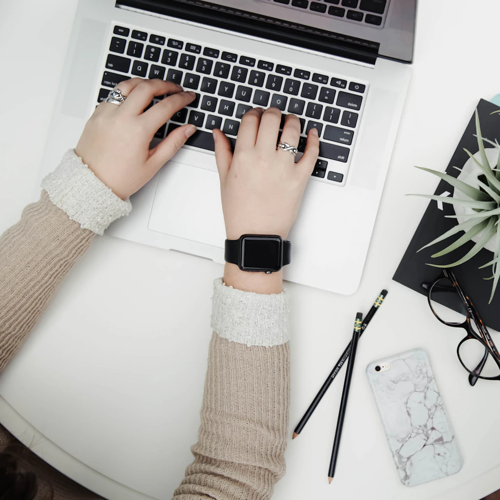 Hands typing on a laptop on a white desk beside a plant